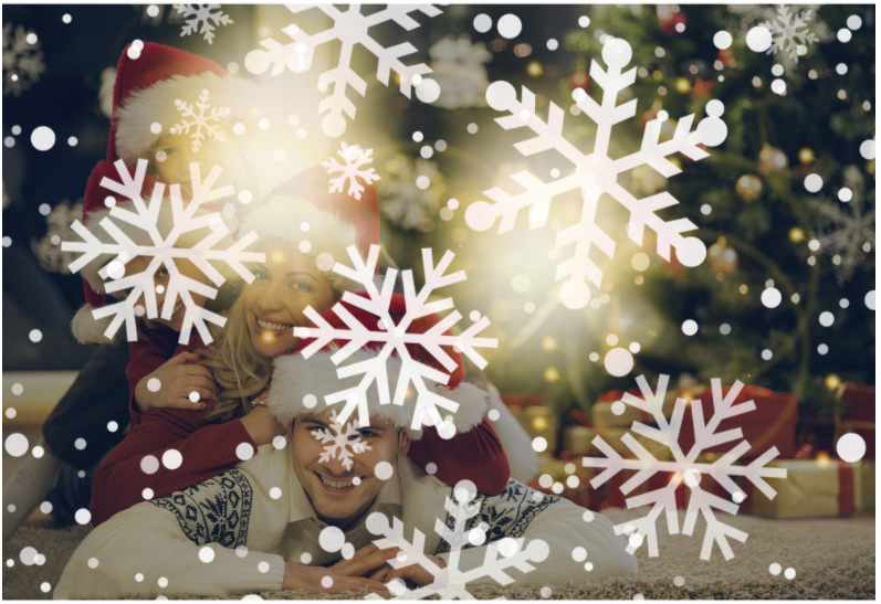 Family in Santa hats by the Christmas tree with snowflakes projected around them